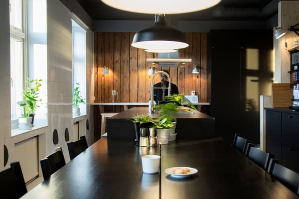 Stort svart köksbord står mitt i köket och förlänger köksön som finns längre in i rummet. 