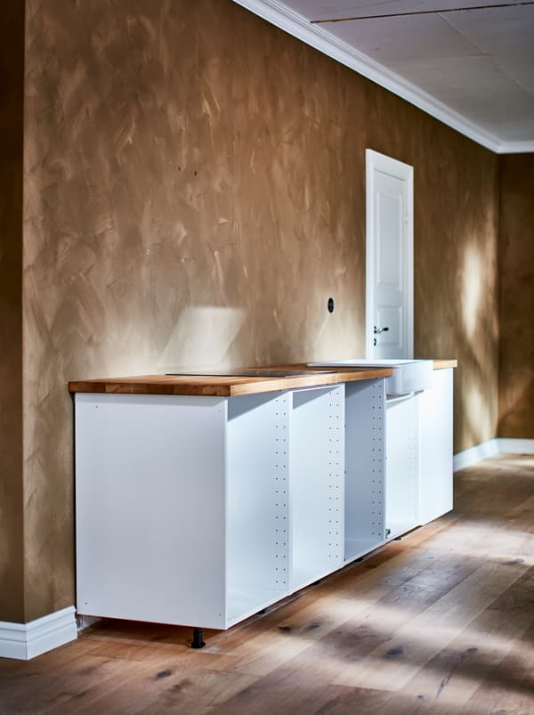 Structure d’armoire inférieure blanche METOD sans porte devant un mur aux teintes brun clair avec fini brossé.