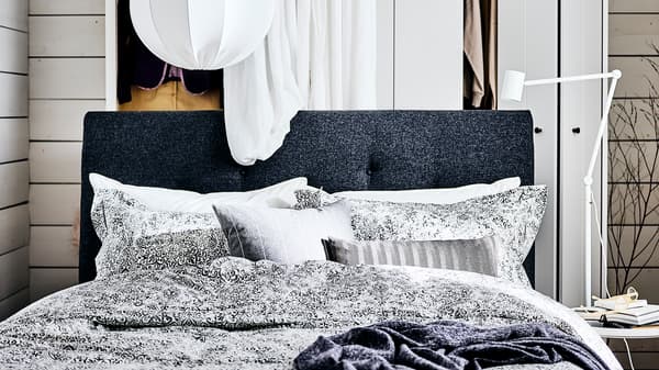 Struttura letto imbottita IDANÄS grigio scuro con una tenda bianca e un armadio bianco dietro. Sopra, una lampada a sospensione bianca - IKEA