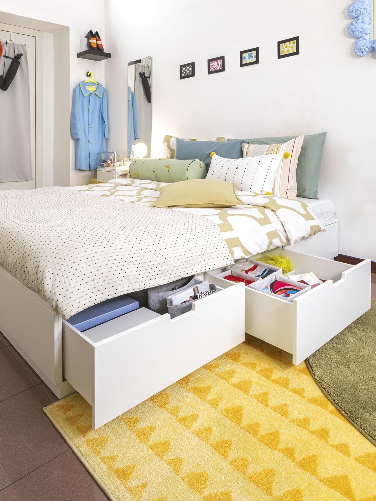 struttura letto NORDLI con cassetti aperti in una camera da letto dalle pareti bianche e con un tappetto giallo. 