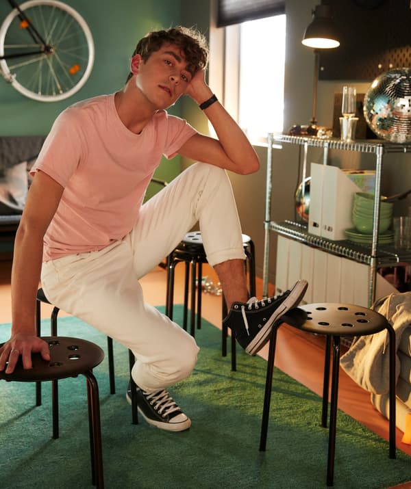 Student siedzi na czarnym stołku, opierając nogę na drugim stołku.