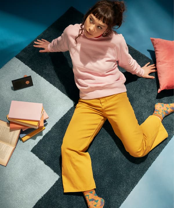 Studentka siedzi na dywanie w zrelaksowanej pozie, w otoczeniu książek i głośnika bezprzewodowego.