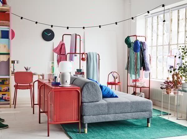Studio aux couleurs vives, avec canapé convertible en gris, commode rouge et deux tapis verts.