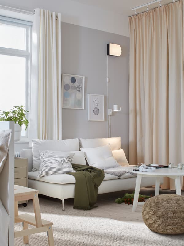 Stue med en lys SÖDERHAMN sofa, et sofabord og en puf. Væggen længst væk har gardiner, der går fra gulv til loft.