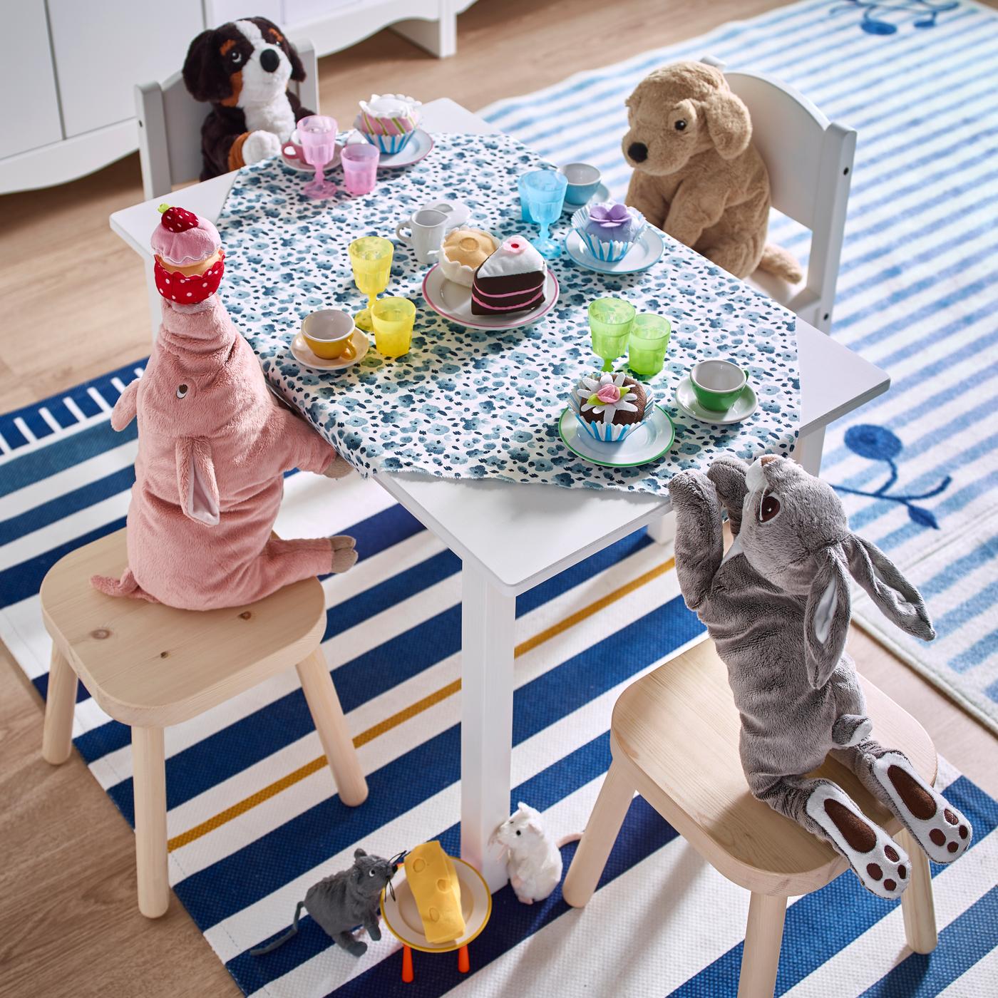 Stuffed animals sitting on chairs and stools around a table having tea