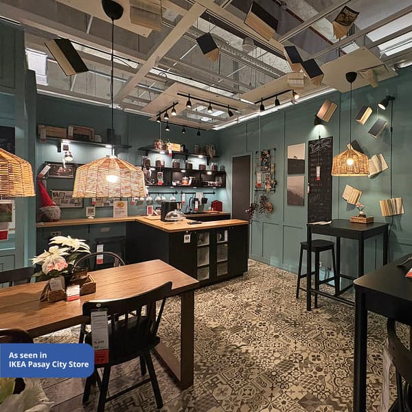 Stylish interior featuring a kitchen area with wooden tables, woven lighting, teal walls, and books hanging from the ceiling. As seen in IKEA Pasay City Store.