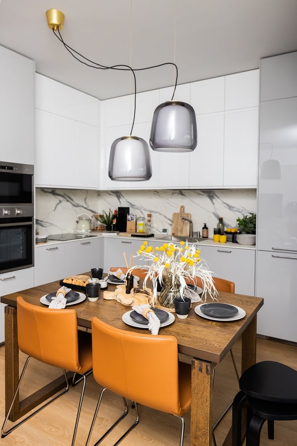 Stylish kitchen with marble backsplash, wooden dining table, orange leather chairs, and modern pendant lights.