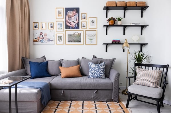 Stylish living room seating area with gray sofa, accent pillows, wall shelves, and floor lamp