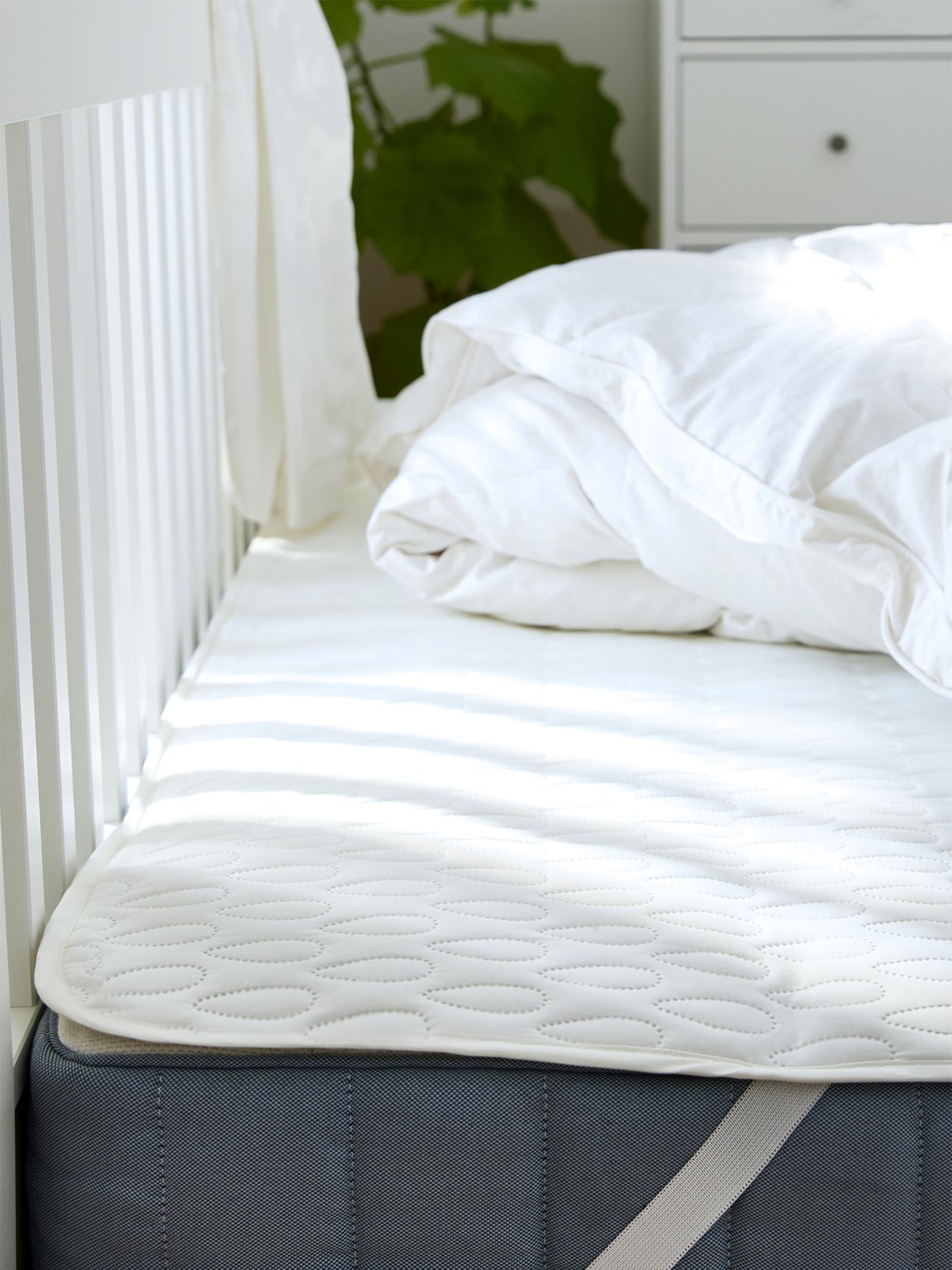 Su una struttura letto c'è un materasso con proteggi-materasso, su cui è appoggiato un piumino stropicciato.