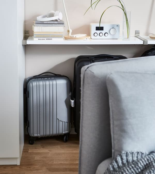 Suitcases stored behind a light grey IKEA VALLENTUNA modular sofa unit and underneath a white mounted shelf.