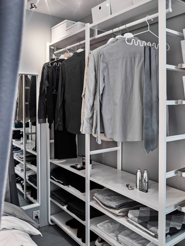 Suits and blazers hanging from a white, open wardrobe system within a small sleeping space.