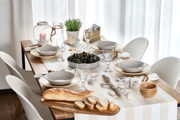 Summer dining table with seashells, bread, candles, glasses and bowls in light natural tones.