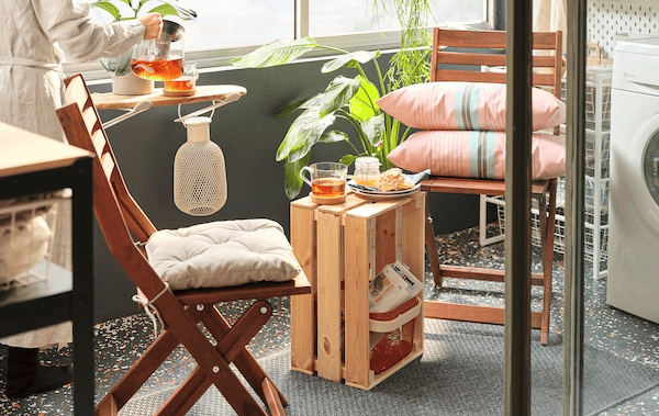 Sunlit balcony coffee nook formed by folding chairs and a KNAGGLIG crate standing on its side as a small table in between.