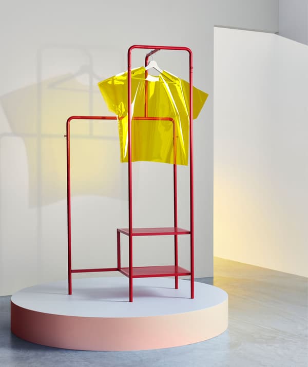 Suport de haine metalic, roșu, așezat pe un podium cu un tricou galben din perspex suspendat de acesta.