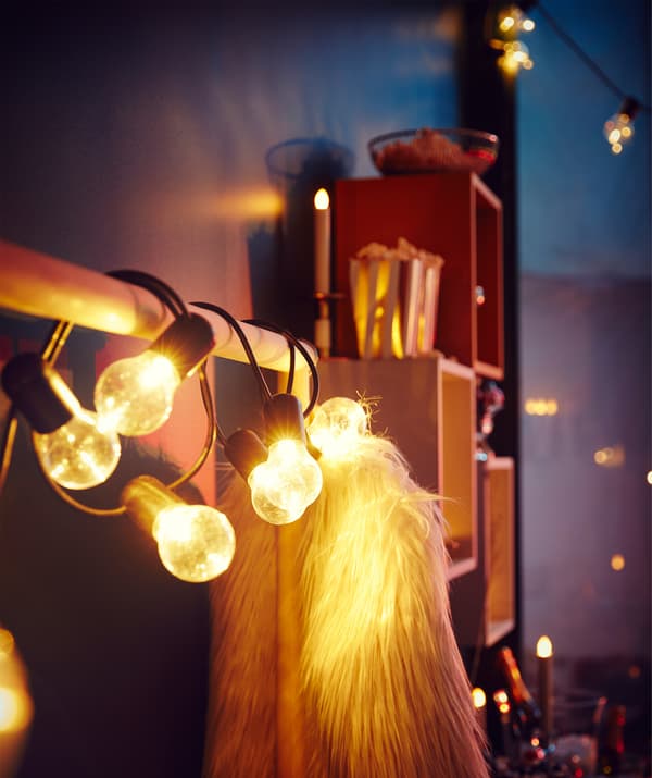 Suporte para cabides colocado junto de uma parede com um casaco peludo festivo pendurado e um sistema de iluminação grande enrolado no varão.