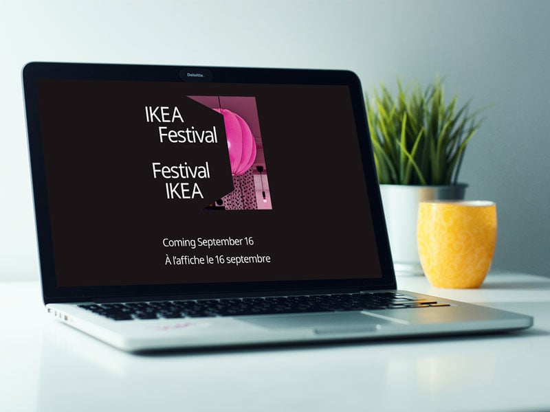Sur un bureau blanc, un ordinateur portable affiche le logo du Festival IKEA et le texte suivant sur un fond noir : « Festival IKEA. À l’affiche le 16 septembre. »