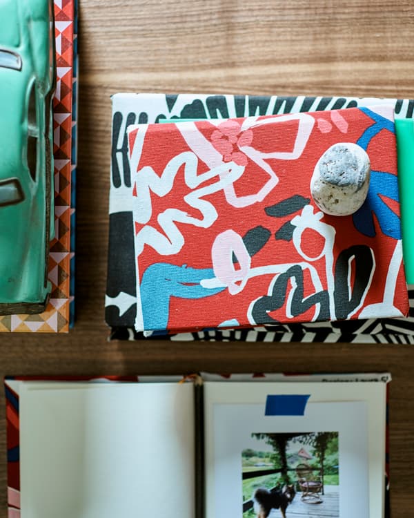 Sur une table en bois, à côté d’une petite voiture verte, des livres recouverts de tissu à motif. Un livre est ouvert à une page sur laquelle une photo est collée.
