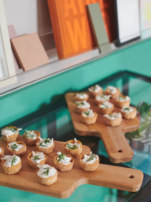 Sur une table en verre, des planches à découper PROPPMÄTT sur lesquelles sont disposées des mini-croustades KRUSTADER garnies.