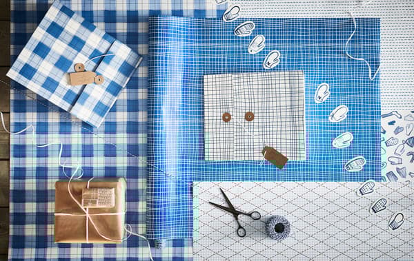 Sur une table, tout le nécessaire pour emballer des cadeaux: papier de différentes couleurs et motifs, ficelle, ciseaux, étiquettes et cadeaux emballés.