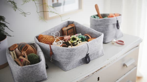 Sur une vieille commode usée sont posés des paniers RAGGISAR en tissu remplis de babioles et de menus objets.