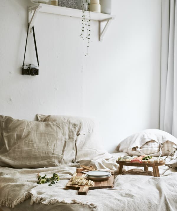 Sushi served on wooden boards on a bed with neutral-coloured bedding and a shelf on the white wall above.