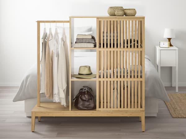 Sustainable NORDKISA bamboo wardrobe in bedroom infront of MALM queen-sized bedframe, showing stacks of neatly stacked clothes, a hat and a duffel bag through one of its open sliding doors. Ironed shirts and other clothing items are also hung on the side rail. 