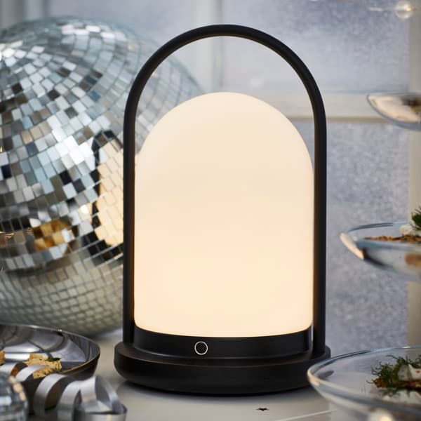 Svart lampa med rund design och vit lysande skärm, placerad bredvid en discokula.