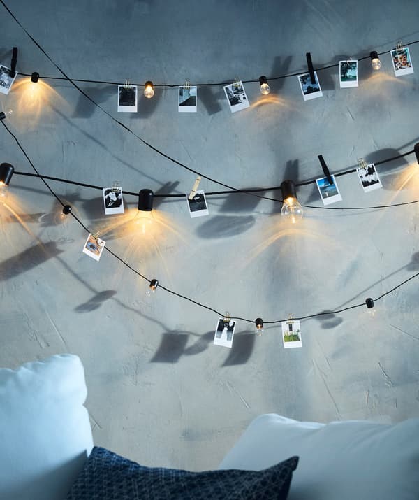 SVARTRÅ LED lighting chains hanging across a grey wall, with small illustrations clipped to the cords between the bulbs.