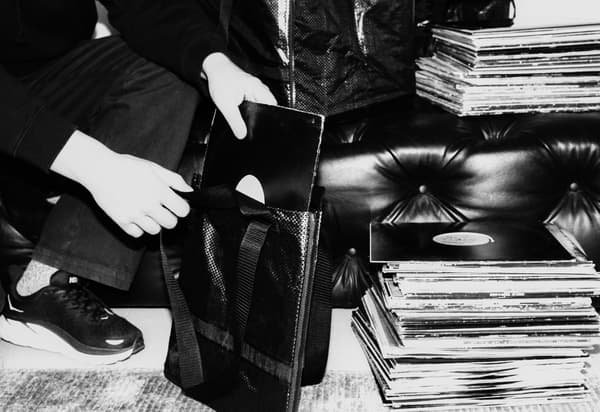 Svartvit bild: En människa sitter på huk och lägger ned vinylskiva i en väska. En hög med vinylskivor står bredvid