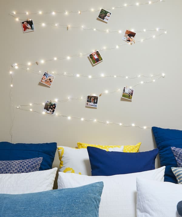 Svetelná reťaz a fotografie na stene nad posteľou plnou vankúšov v útulnej a osobnej spálni.