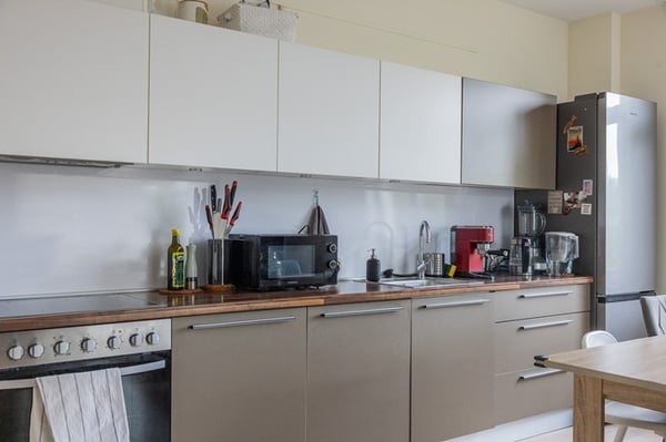 Светлая современная кухня с белыми шкафами, столешницей, бытовой техникой и кухонными принадлежностями.