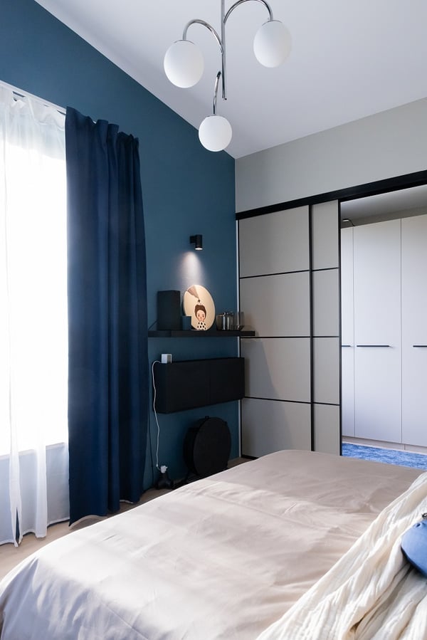 Светлая спальня с синей акцентной стеной, большим окном и современным потолочным светильником