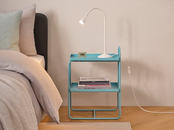 Svetlo-modrý nočný stolík s lampou na vrchu a knižkami na spodnej polici