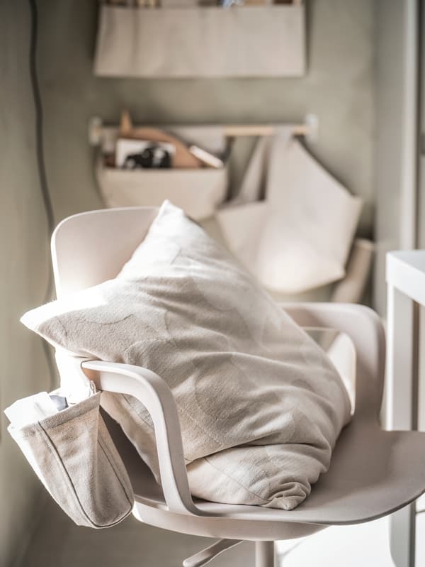 Svetlobéžová miestnosť, v popredí sa nachádza béžová otočná stolička ODGER. Na stene v pozadí sú umiestnené tri závesné úložné diely NEREBY prírodnej farby, ďalší je pripevnený k opierke na ruky na otočnej stoličke.