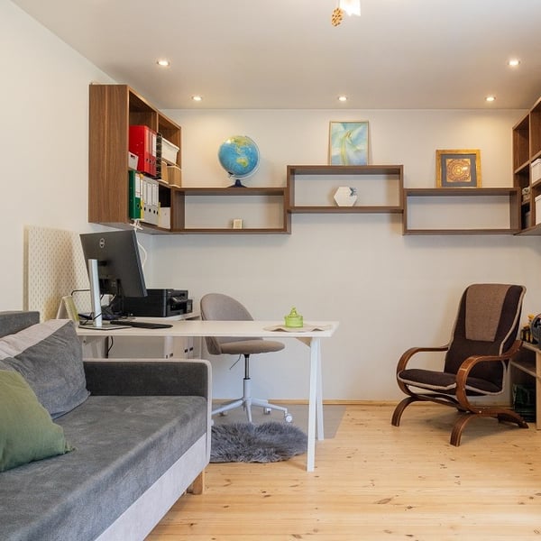 Светлый домашний офис с письменным столом, стеллажами, компьютером, диваном и деревянным полом