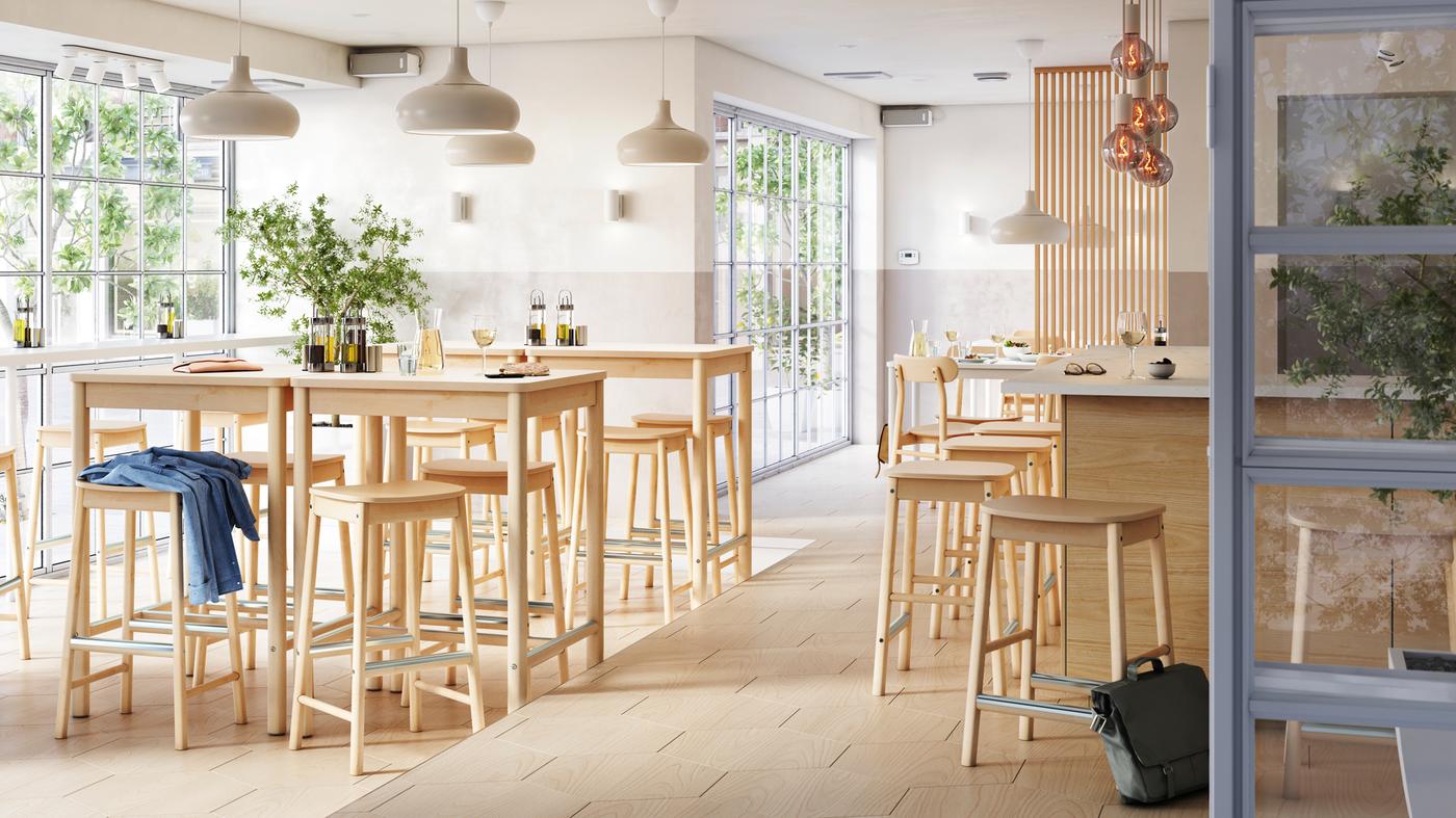Svijetao i prozračan bar s više zona s RÖNNINGE barskim stolcima i stolovima od breze uz prozor te sjedištima u sredini bara.