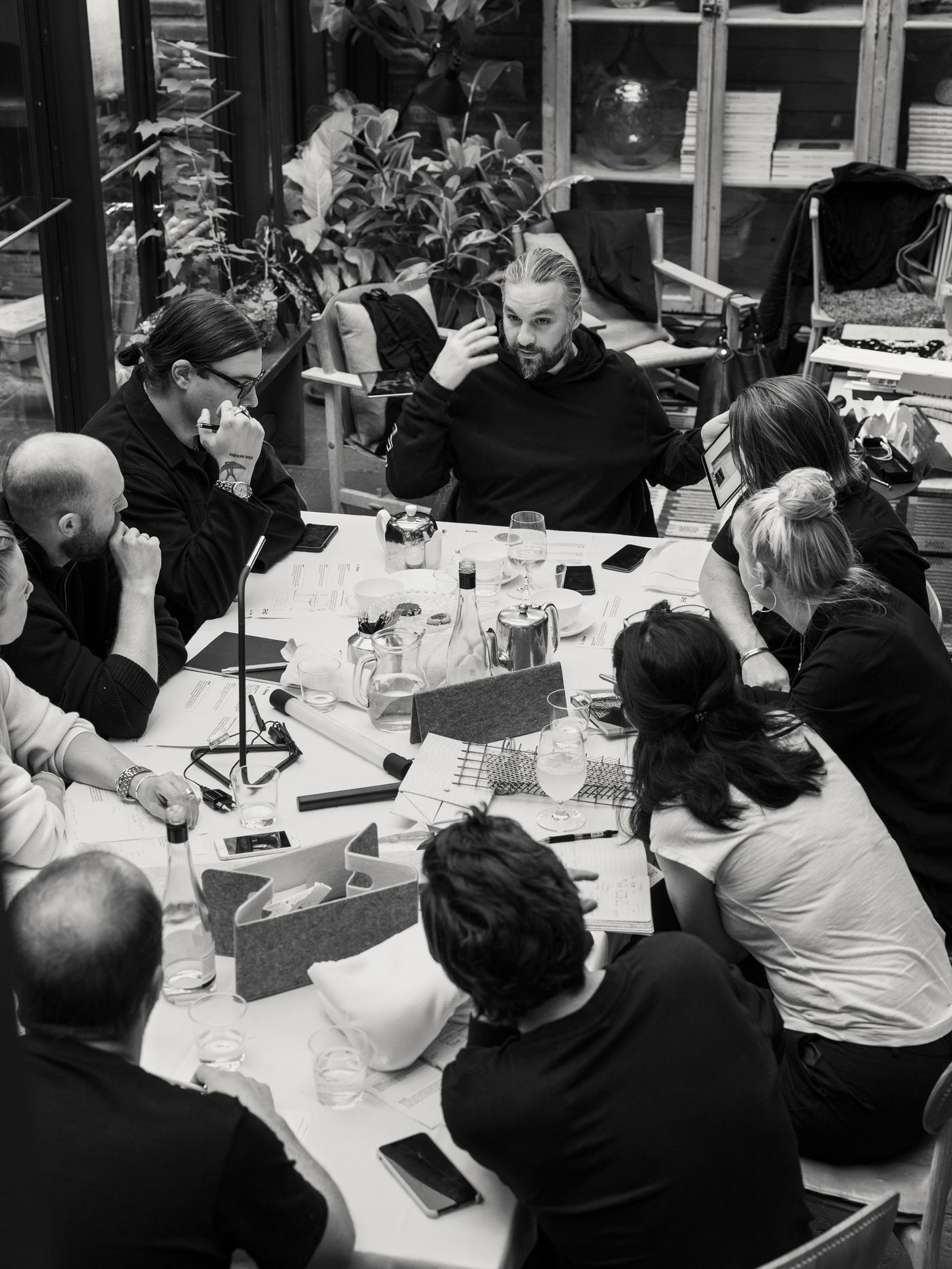 Swedish House Mafia taldeko kideak eta IKEA-ko diseinatzaileak material, paper eta edalontziz beteriko mahai baten inguruan. Atzealdean landareak ikus daitezke.