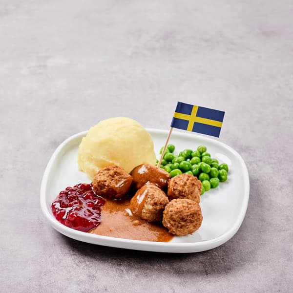 Swedish meatballs with mashed potatoes, peas, gravy and lingonberry jam on a white plate.				