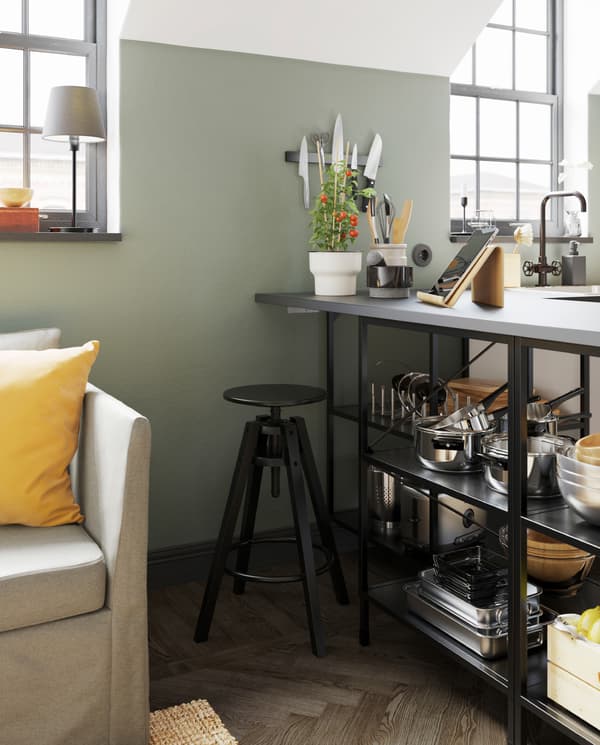 صوفا بيج، وسجادة من الجوت، وسطح عمل رمادي، ومقعد مرتفع أسود، وجهاز لوحي على حامل، ونبات طماطم في آنية نباتات.