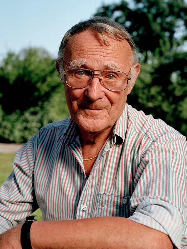 صورة لمؤسس ايكيا Ingvar Kamprad، وهو يبتسم في مكان مفتوح ويرتدي قميصًا مخططًا باللون الوردي والأبيض والأخضر.