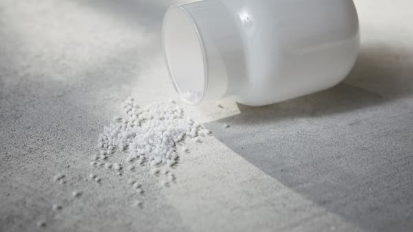 Synthetic pellets spilling out of a glass container on fabric. 