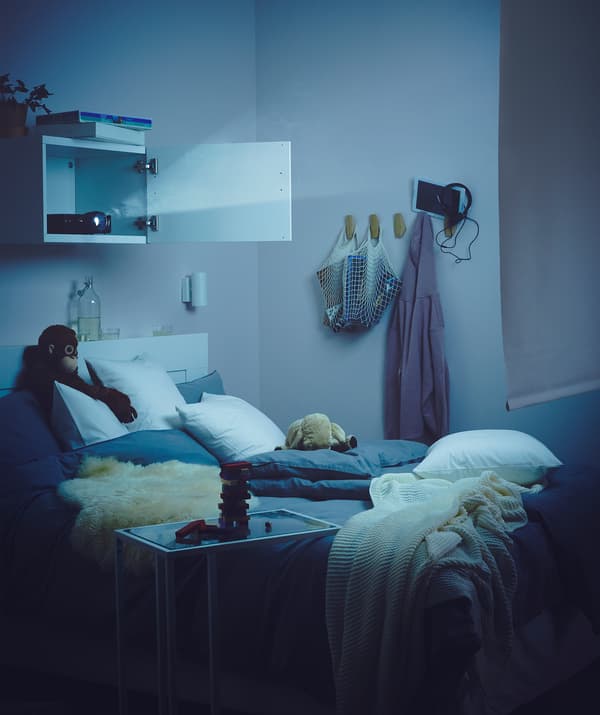 Sypialnia słabo oświetlona światłem z projektora ustawionego w szafce ściennej nad łóżkiem, którego promień jest skierowany na roletę zawieszoną w poprzek pokoju.