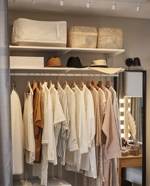 Système de rangement ouvert avec des vêtements suspendus sur une tringle. Sacs de rangement, boîtes et chapeaux rangés sur des tablettes au-dessus.