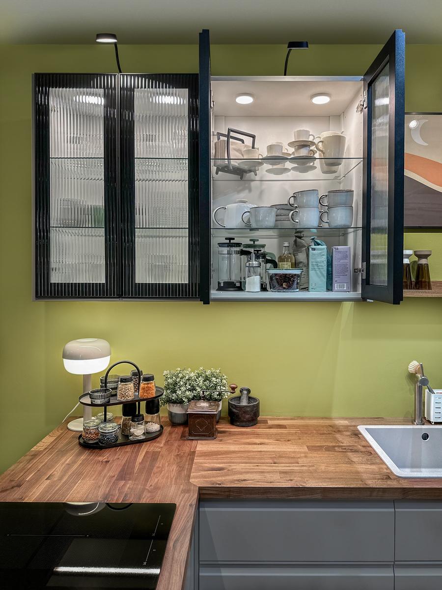 Szafka wisząca w fornie wytryny. Drzwiczki od szafki są z ryflowanego szkła w czawnej ramie.