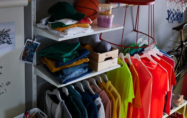 T-shirts on hangers, hung on the bottom steel frame of a red IKEA TRANARÖ stool attached to the wall.