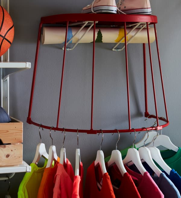 T-shirts on hangers, hung on the bottom steel frame of a red IKEA TRANARÖ stool attached to the wall.