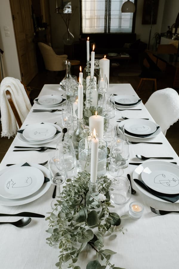 Table à manger dressée avec de la vaisselle blanch et un centre de table végétal et des bougies