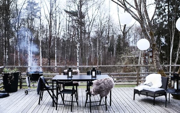 Table à manger et chaises sur une terrasse en bois avec barbecue allumé dans le fond