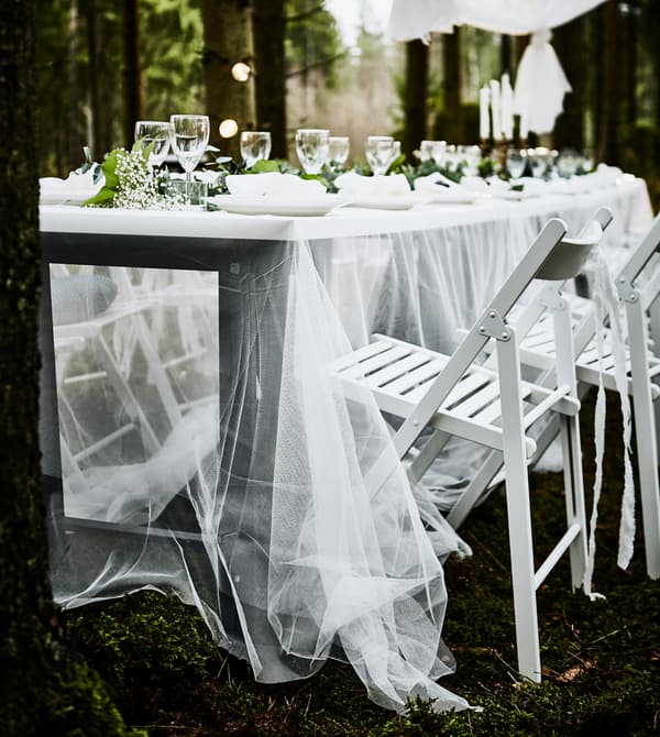 Table avec plateau blanc et fin voilage en guise de nappe, avec chaises pliantes blanches