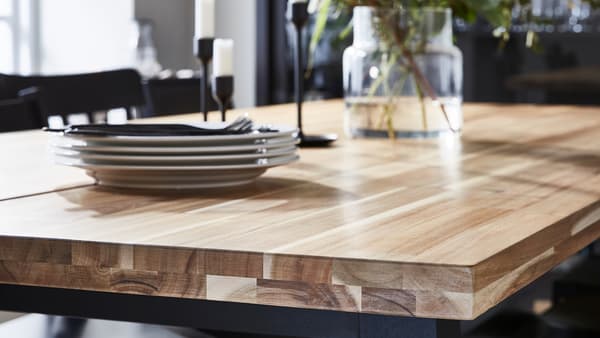 Table avec plateau bois aux veines apparentes sur lequel sont posés une pile d’assiettes, des bougeoirs et un vase.